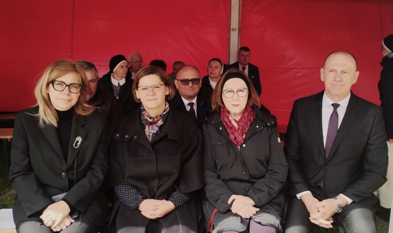Przedstawiciele włądz państwowych i samorządowych - 4 osoby - siedzą na ławce pod czerwonym namiotem. 